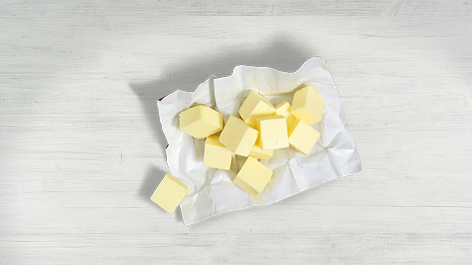 Cubed butter on parchment paper on a wooden surface.