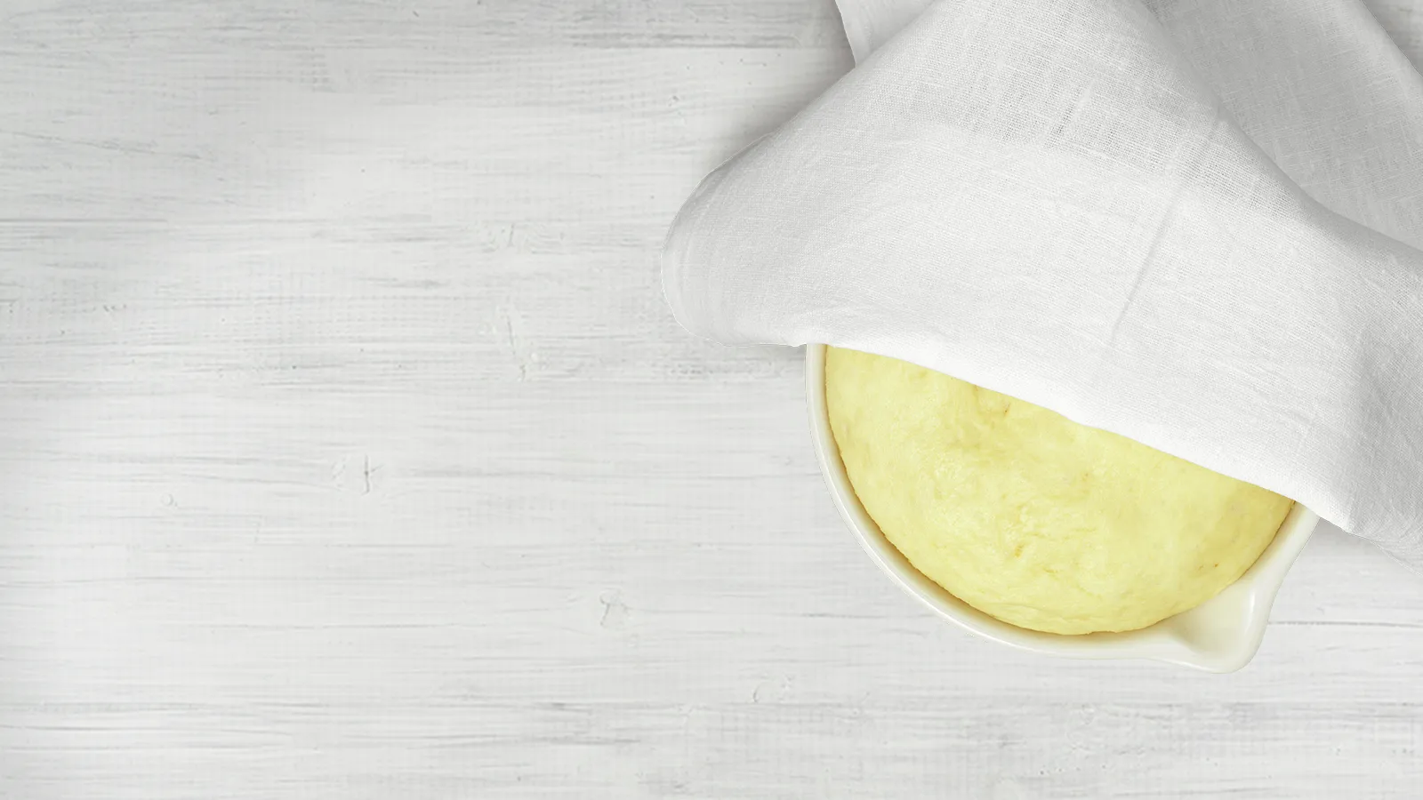 White cloth covering a dough in a bowl on a wooden surface.
