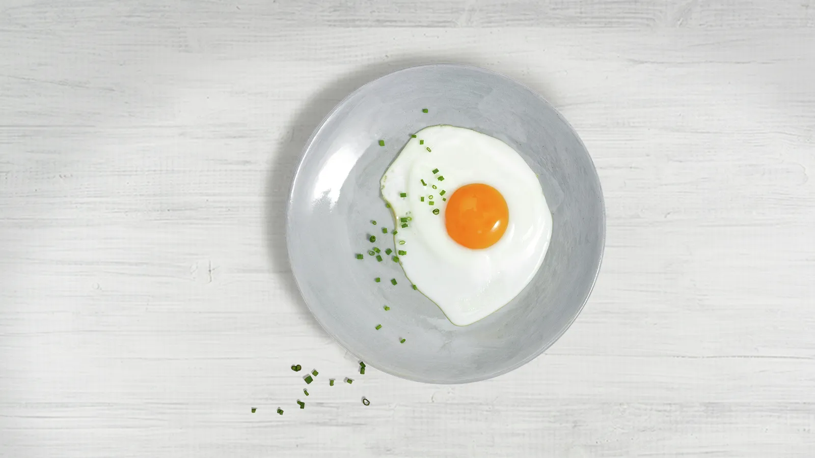 sunny side egg on a plate with scattered herbs and spices on a wooden surface.