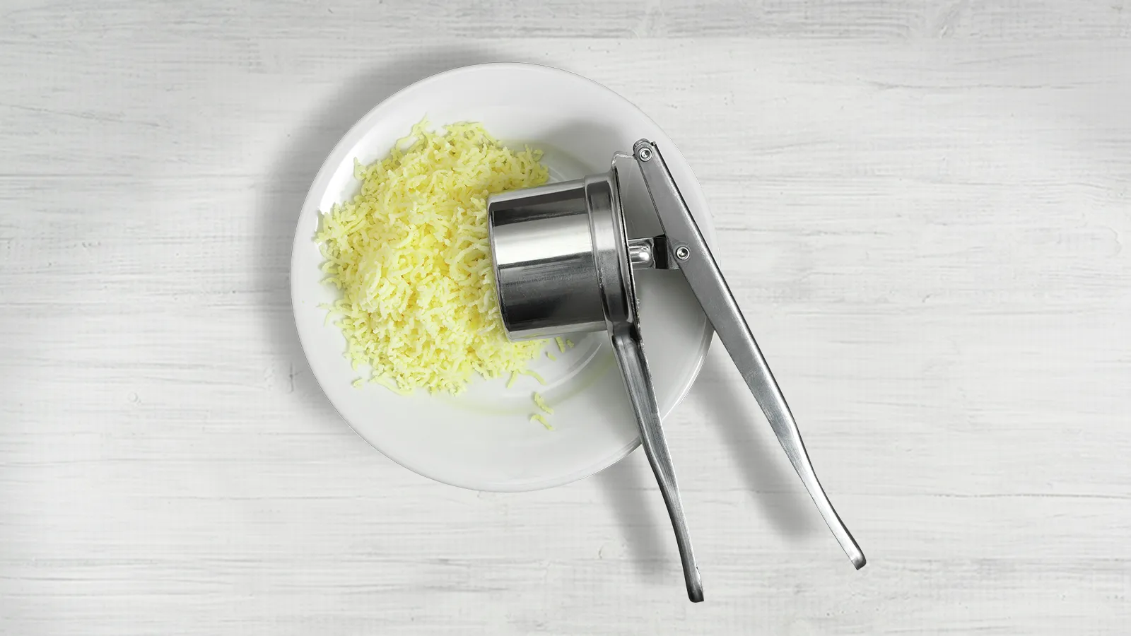 Plate with grated potato, grater tool on white wooden surface.