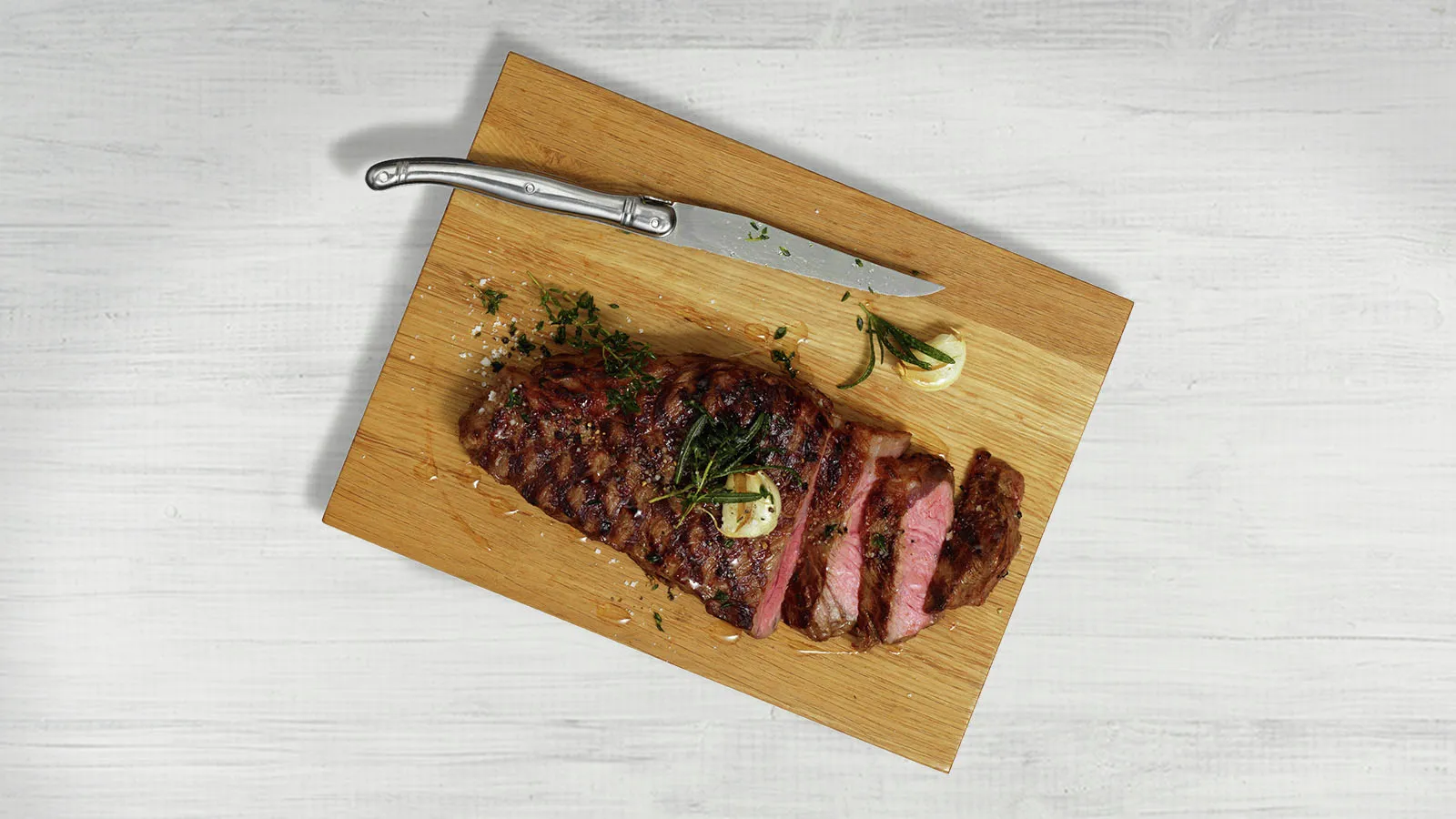 Grilled steak on wooden cutting board with herbs and knife.