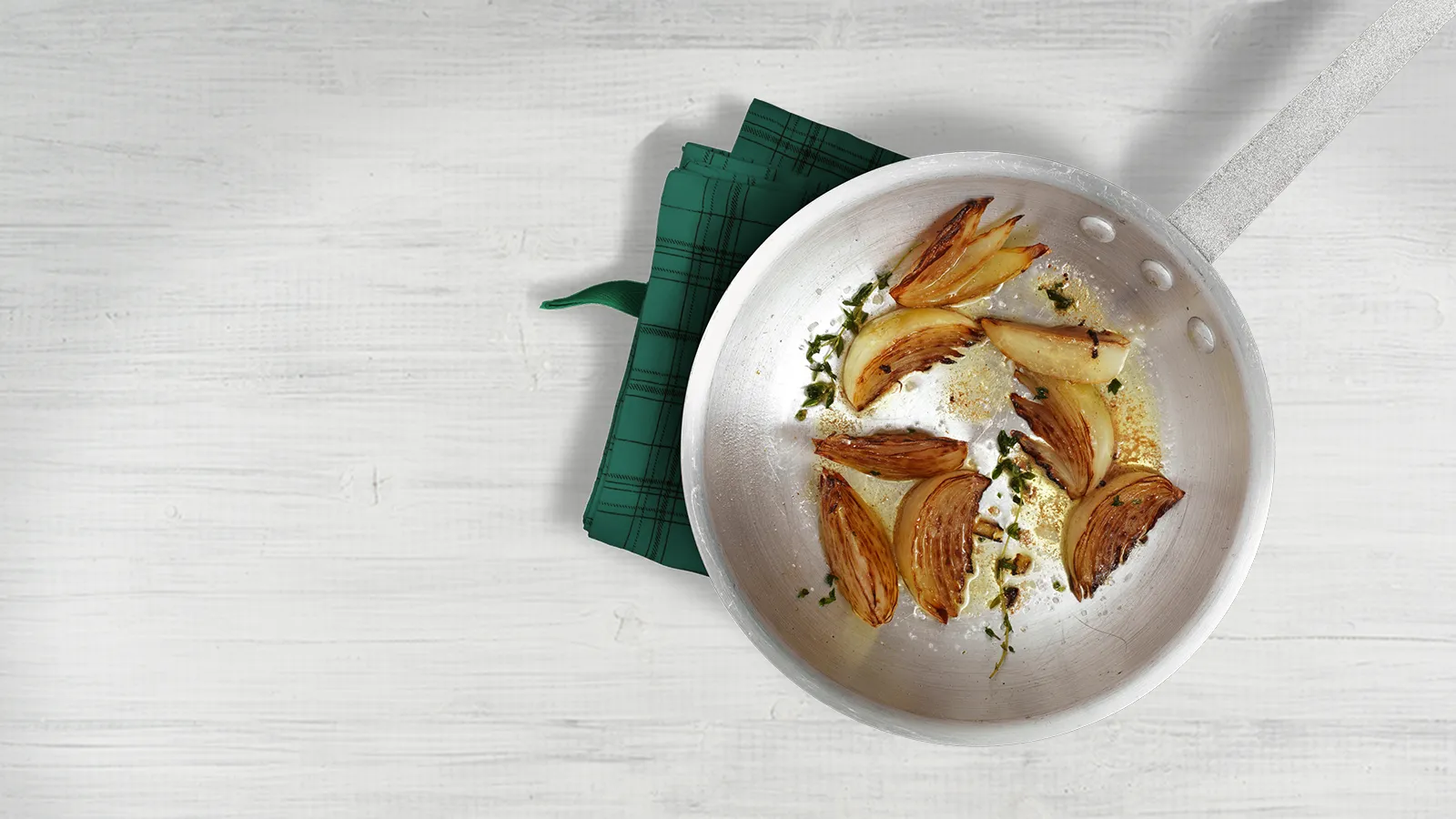 Plate with roasted pears, crumbled cheese, and green napkin on white wooden surface.