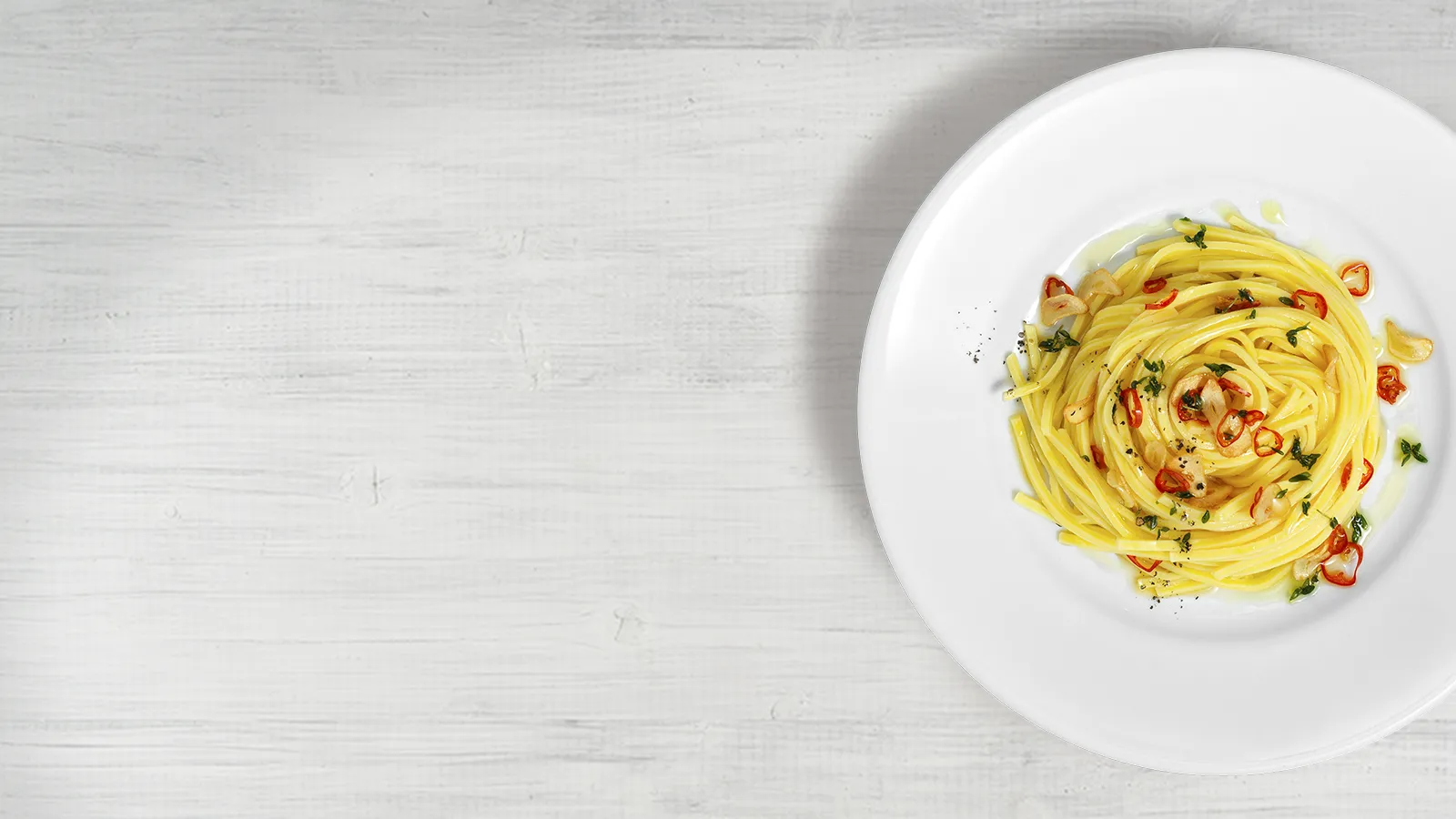 Plate of freshly prepared pasta with tomato sauce and garnishes on a white wooden background.