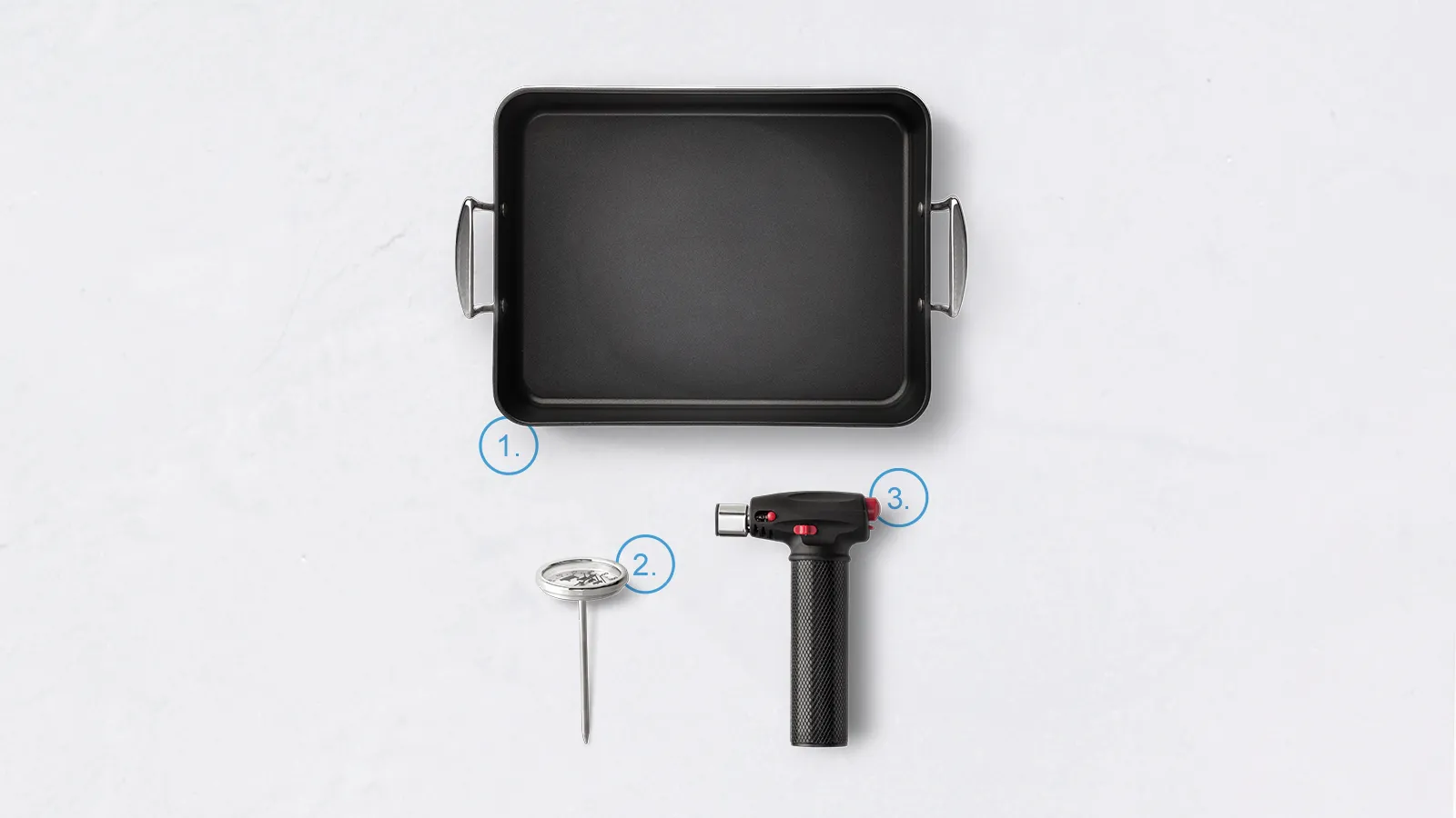 Casserole Dish, meat thermometer, and Blowtorch on a white background.