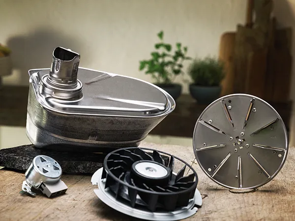 Metal kitchen appliance parts including a food processor blade, fan, and other components on a wooden surface.