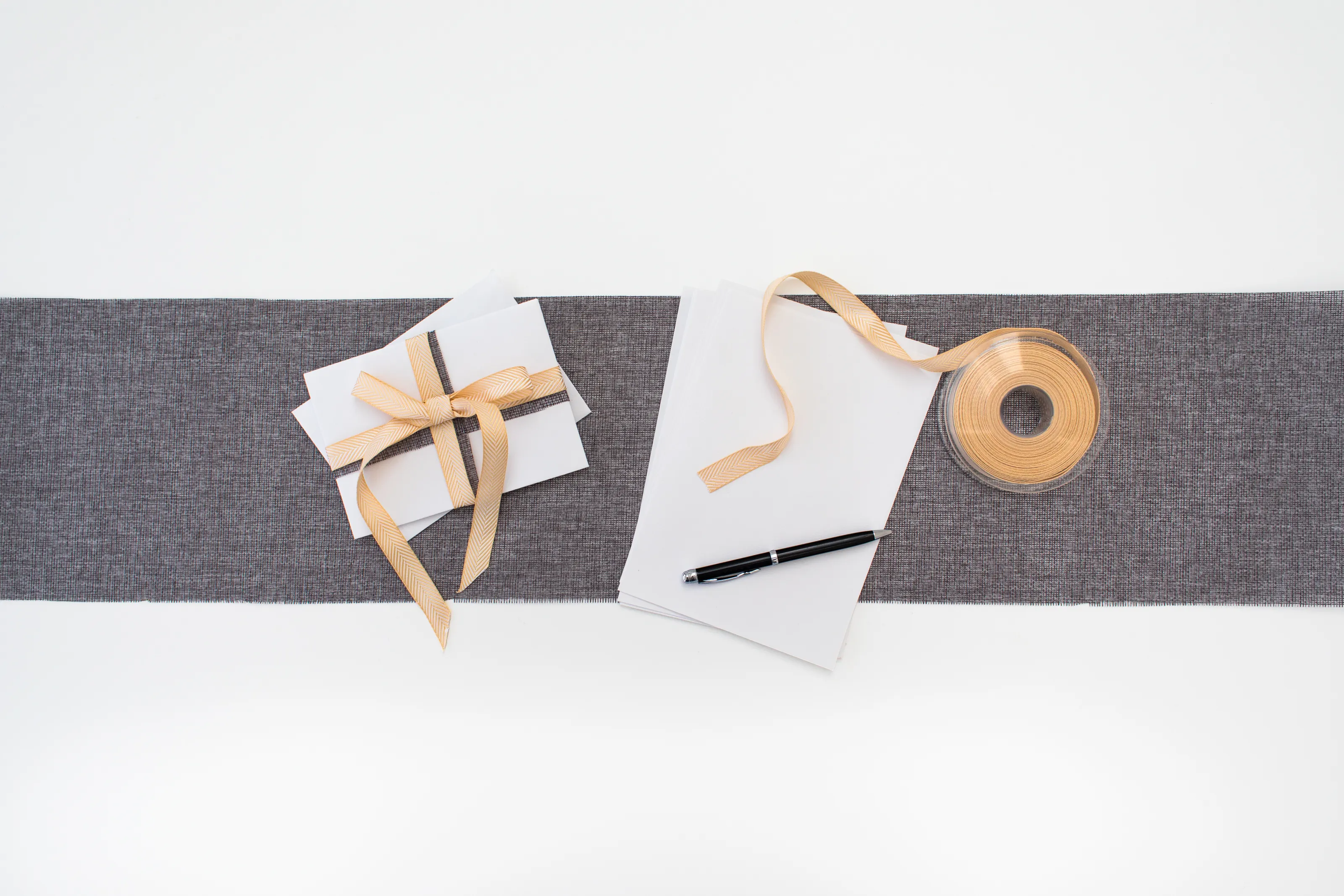 Gift cards with a ribbon, blank paper, and pen on a gray fabric strip.