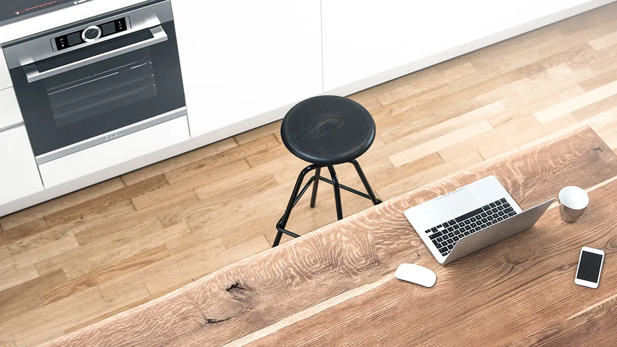 Vogelperspektive einer modernen Küche mit hellem Holzfußboden, einer weißen Küchenzeile samt integriertem Bosch Backofen und einem rustikalen Holztisch mit Laptop im Vordergrund.