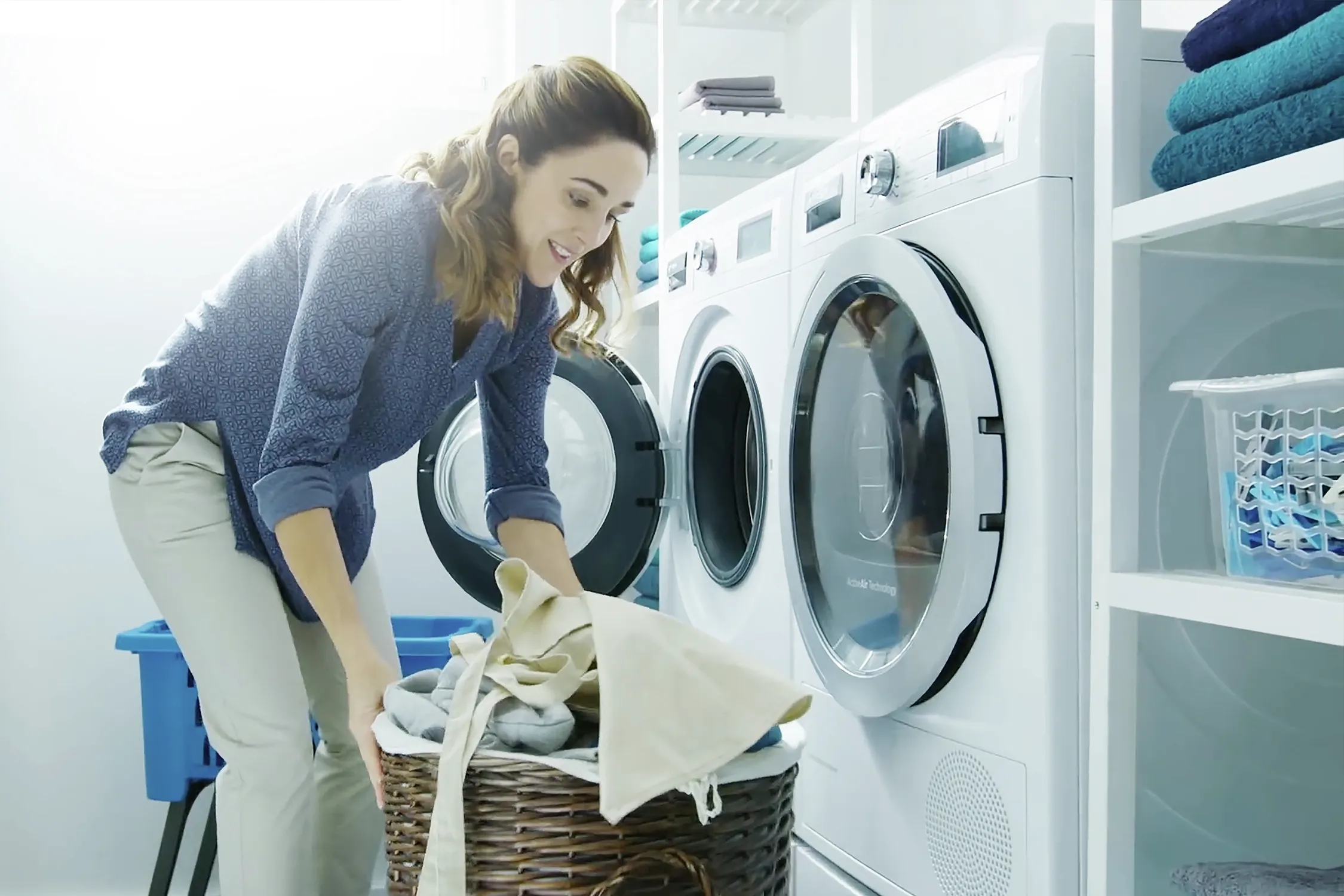 Woman loading laundry into Bosch front-load washer, laundry basket in foreground.