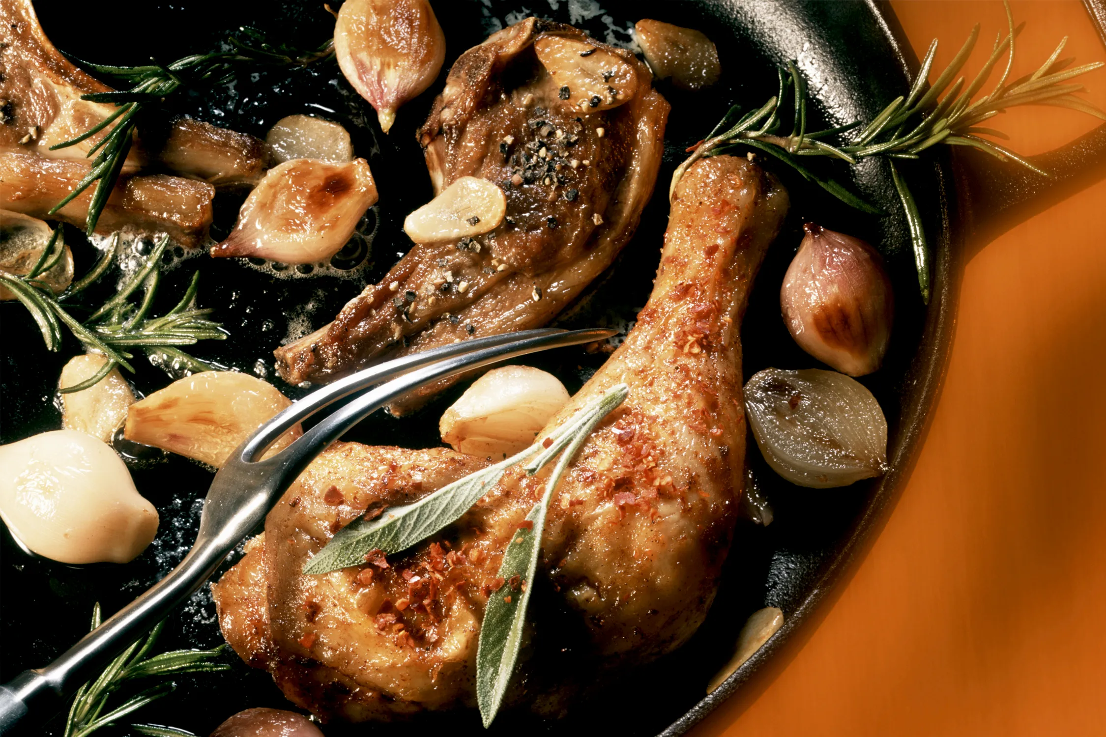 Roasted tavuk bacakları, patatesler ve koyu bir arka plan üzerinde otlar.