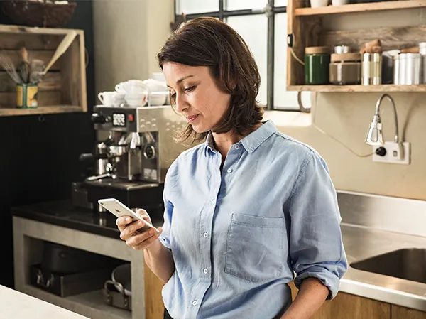 Woman in kitchen using smartphone, standing near coffee machine.