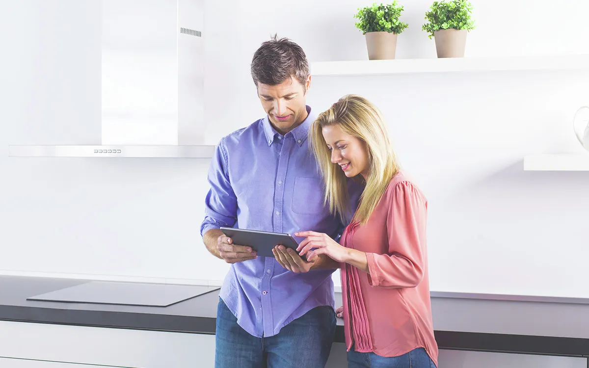 Mann und Frau informieren sich lächelnd auf einem Tablet in ihrer hellen, modernen Küche