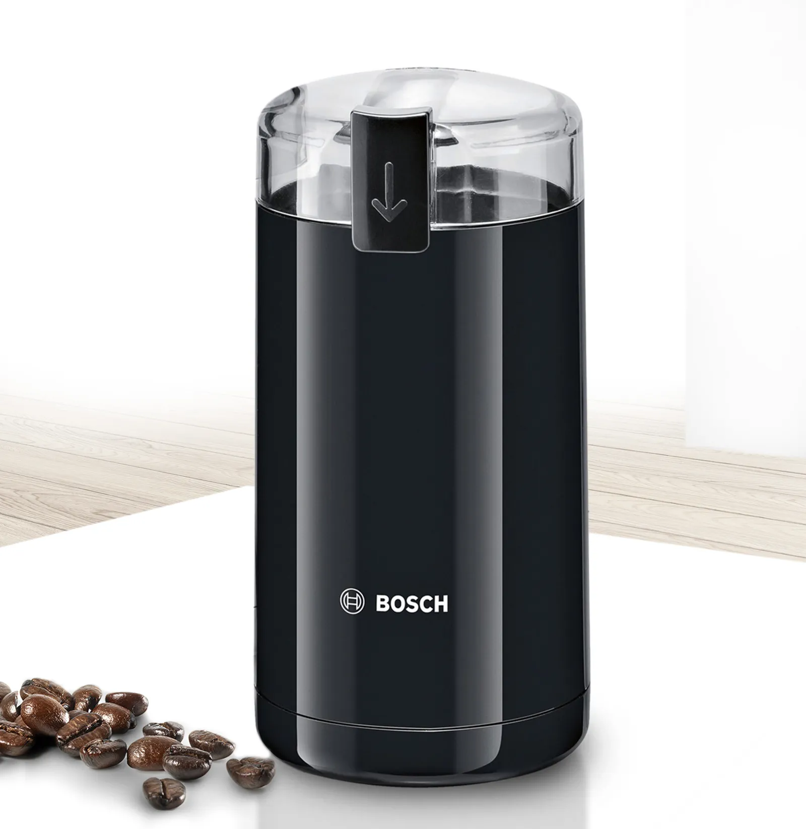 Molinillo de café eléctrico Bosch de color negro con tapa transparente, mostrado junto a granos de café esparcidos.