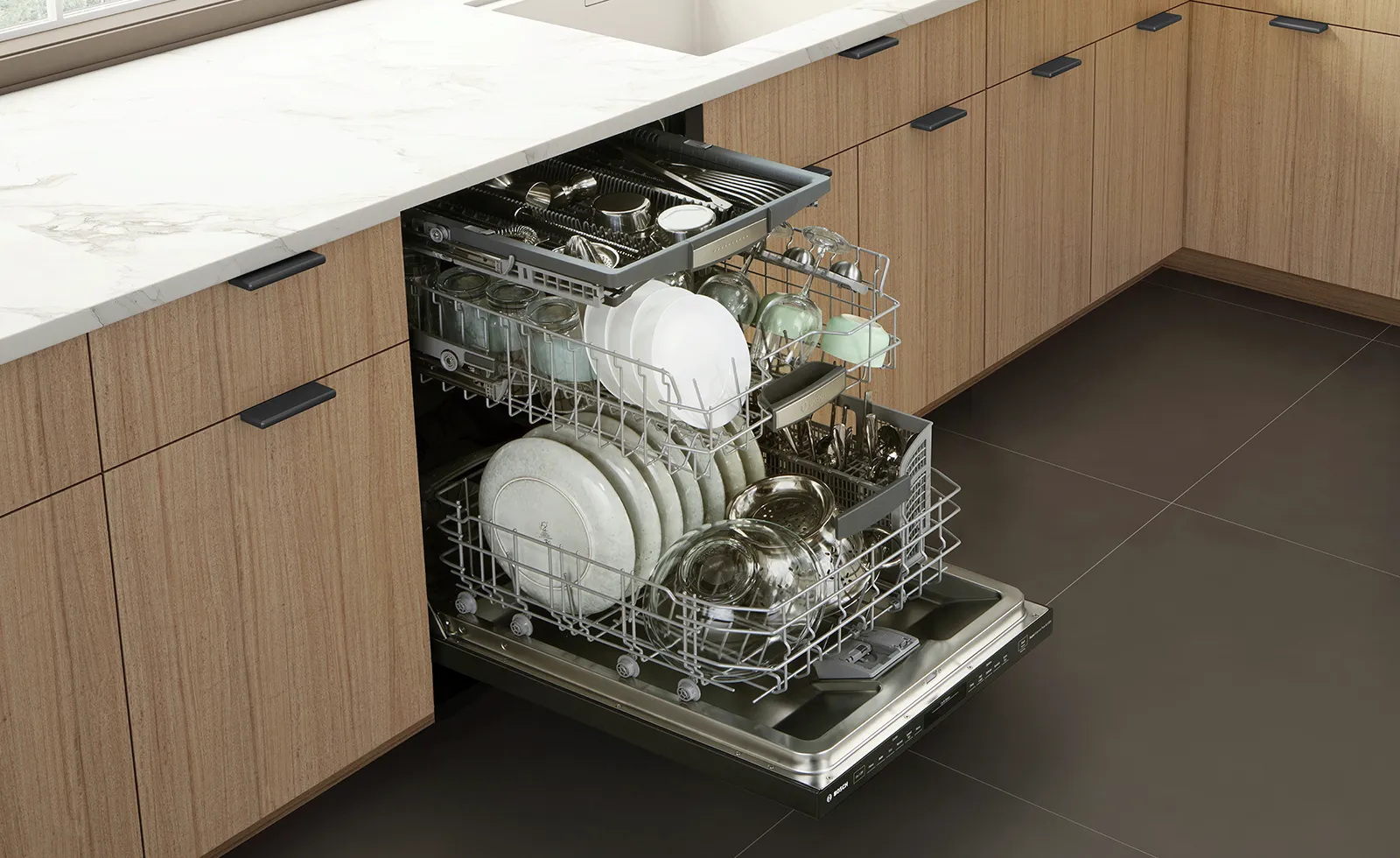 Open Bosch dishwasher in a modern kitchen with plates, glasses, and utensils neatly arranged.
