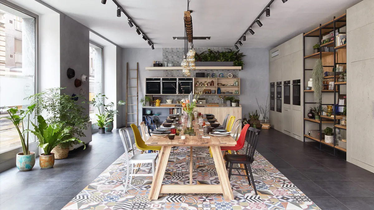 Ampia cucina moderna con tavolo in legno, sedie colorate, scaffali e piante in vaso.