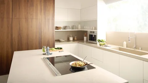 Modern kitchen with an induction cooktop on an island, wood cabinets, and white counters.