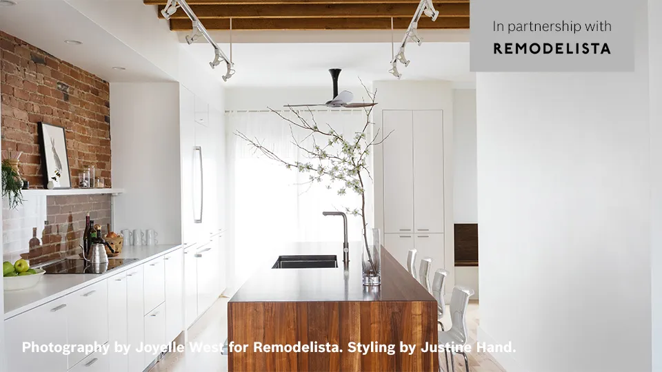 Modern kitchen with a wooden island, white cabinets, and decorative plant branch.