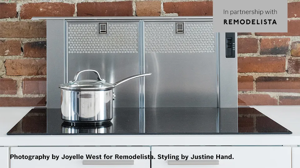 Stainless steel pot on a Bosch electric stove with a metal backsplash against a brick wall.
