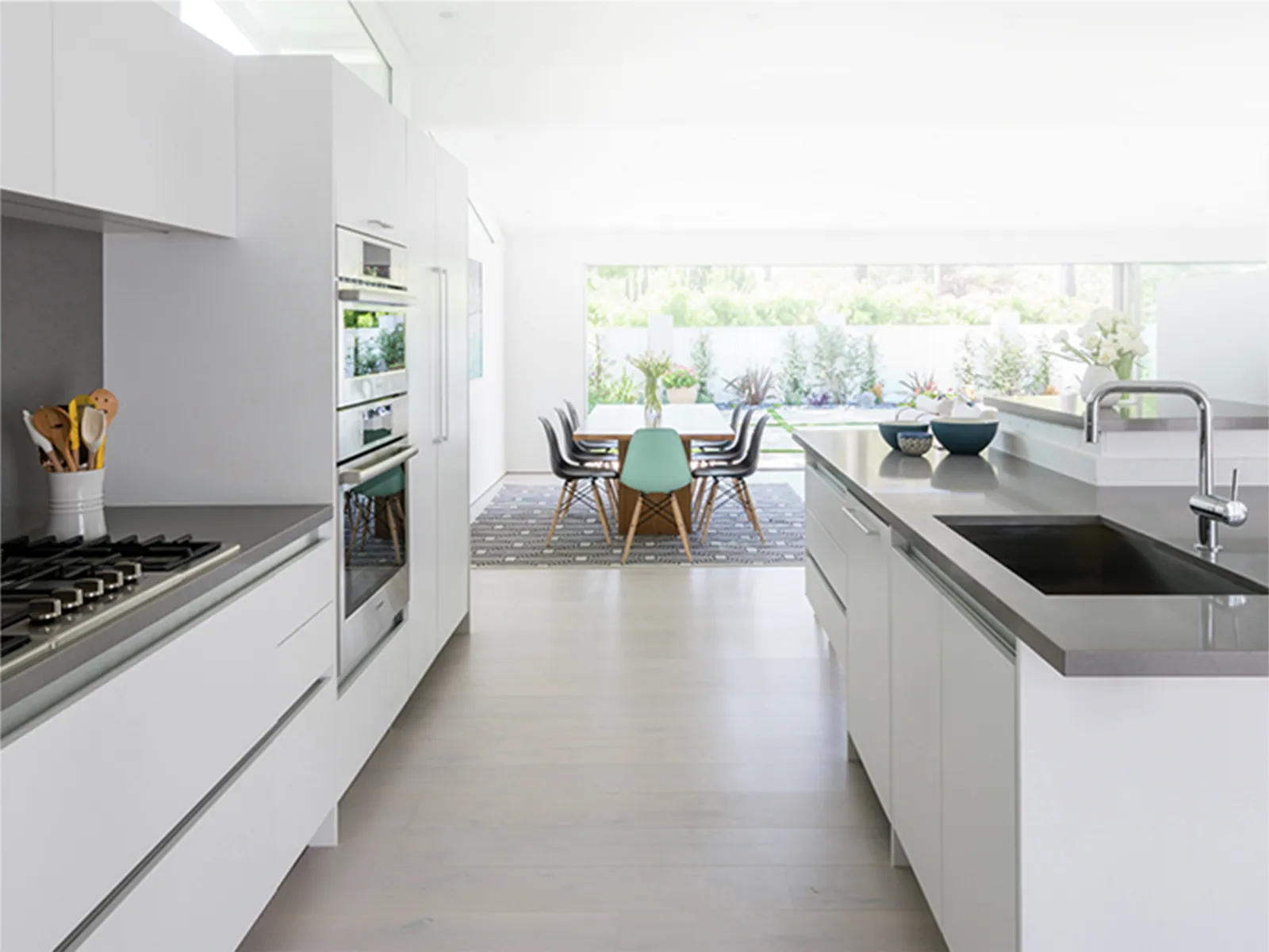Modern kitchen with white cabinets, Bosch double wall oven, Bosch gas stove top, and a view of a dining table outside.