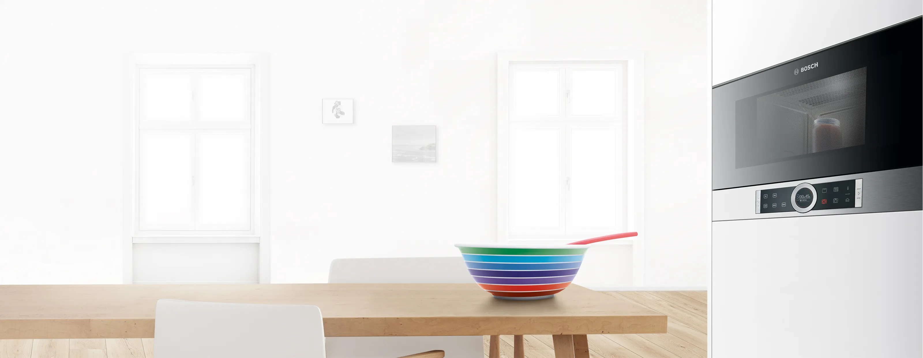 Sleek Bosch microwave oven, colourful bowls, and wooden table in modern kitchen setting.