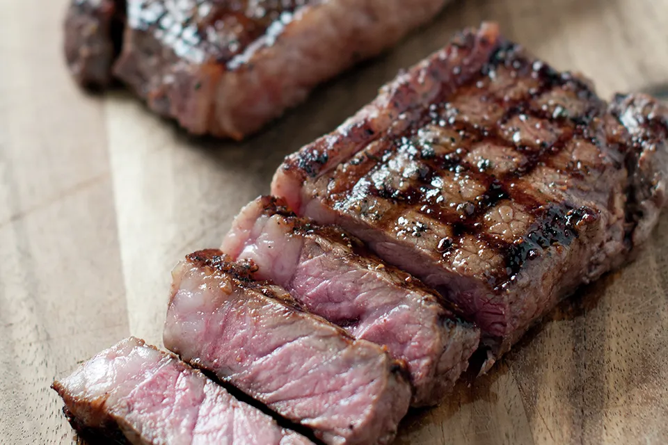 Grilled steak with caramelized surface, sliced on wooden board.