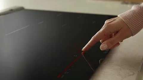 A hand touching the control panel of a modern Bosch induction cooktop on a kitchen counter.