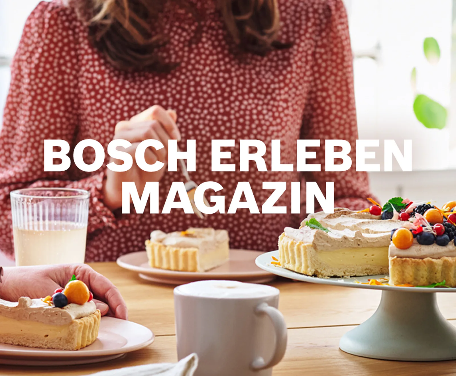 Eine Person am Kaffeetisch schneidet eine mit frischen Früchten dekorierte Tarte an, im Vordergrund stehen Kaffeetassen und Kuchenstücke auf Tellern.