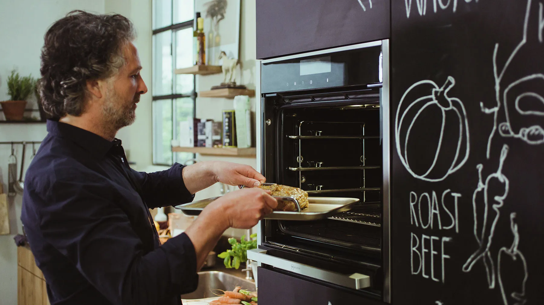 Man placing food in oven, kitchen with chalkboard menu, cooking appliances.