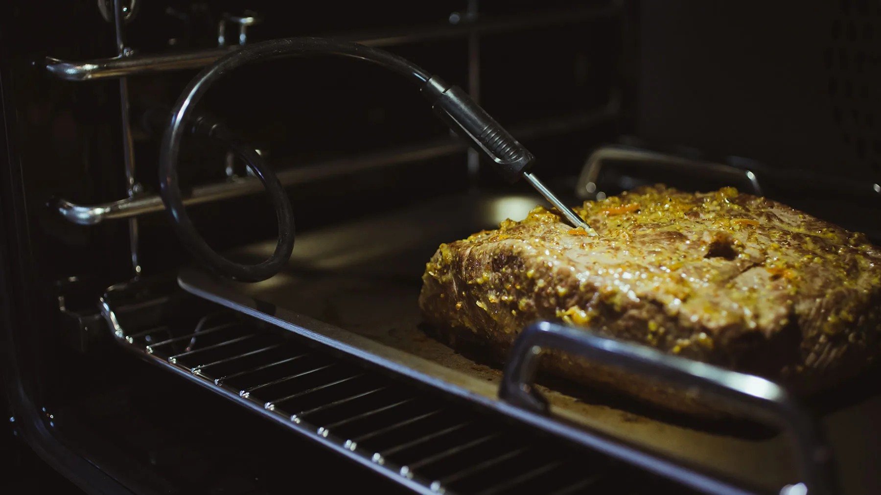 Baked meatloaf dish in oven, with cooking utensils visible.