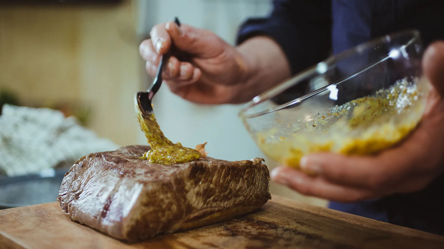 Hands preparing a steak dish, cutting into a seared steak on a wooden cutting board.