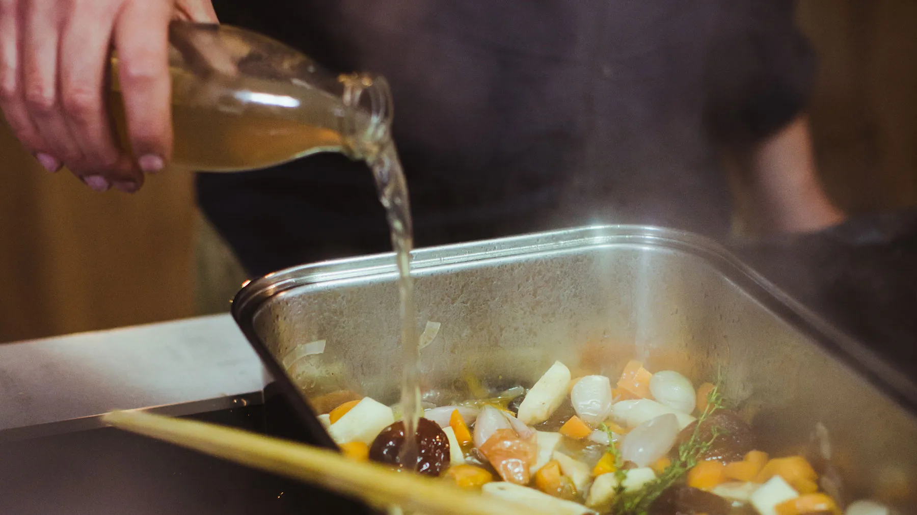 Person pouring stock over roasting vegetables