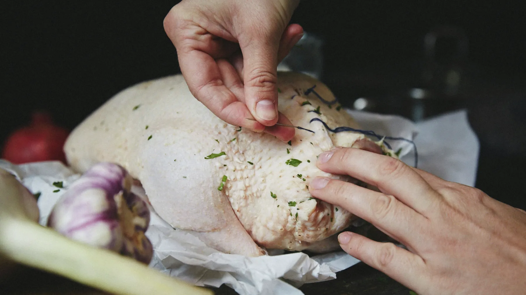Hands preparing a whole chicken, seasoning it with herbs and spices, ready for cooking.