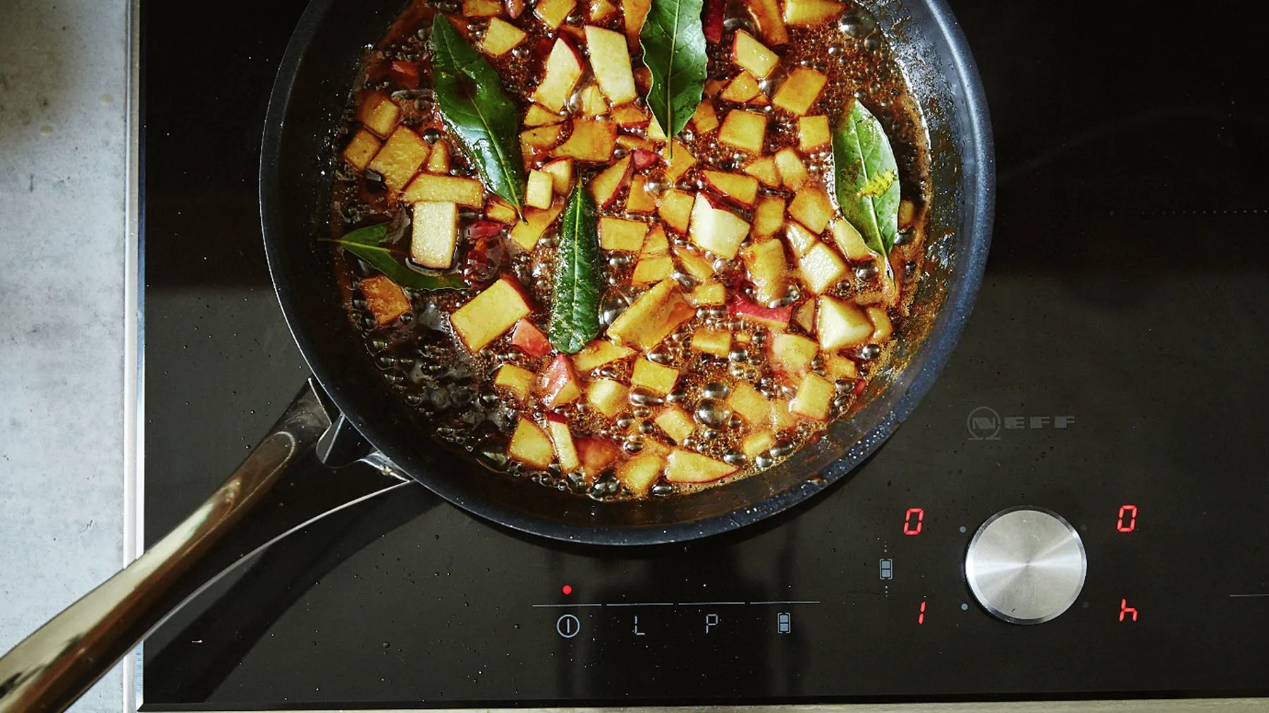 Sizzling pan with diced potatoes, spices, and herbs on a stovetop.