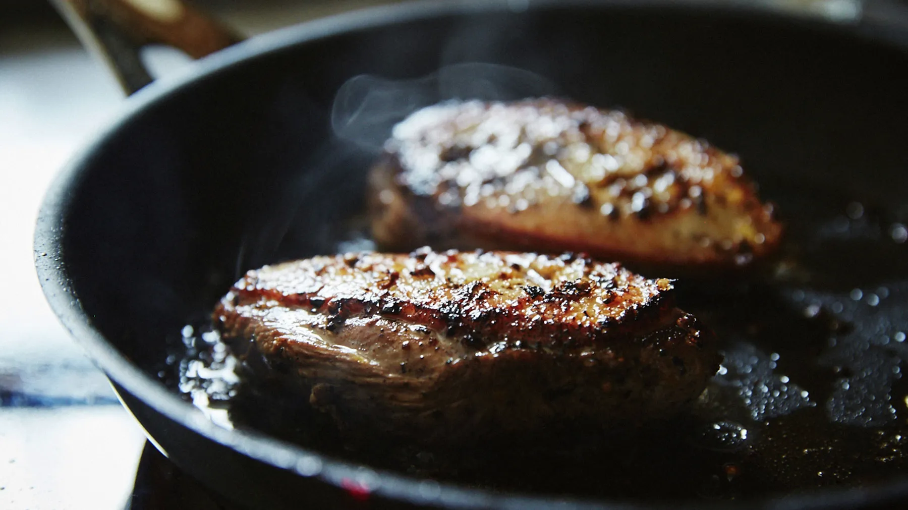 Sizzling steaks in a cast-iron pan, with a crispy, caramelized crust and a smoky aroma.