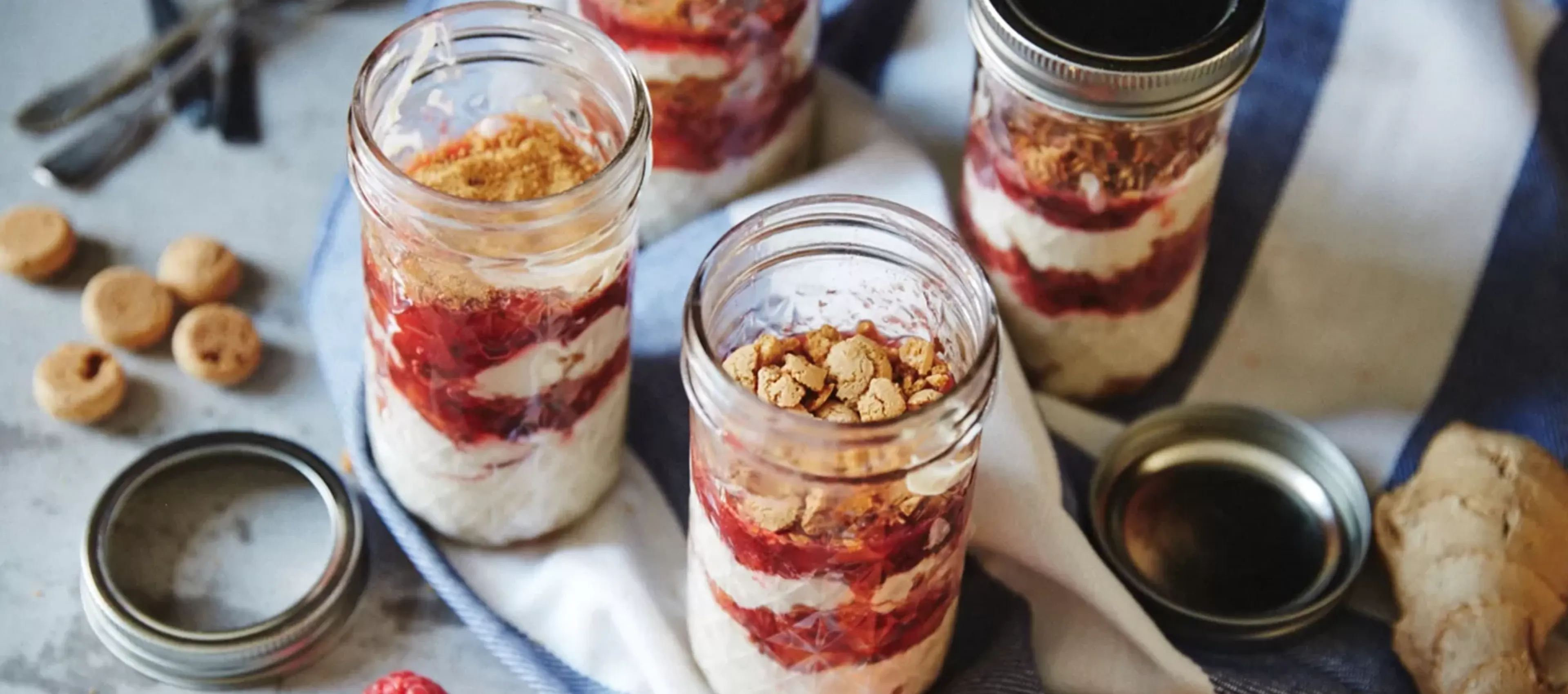 Layered dessert jars with fruit, nuts, and whipped cream on a rustic table.