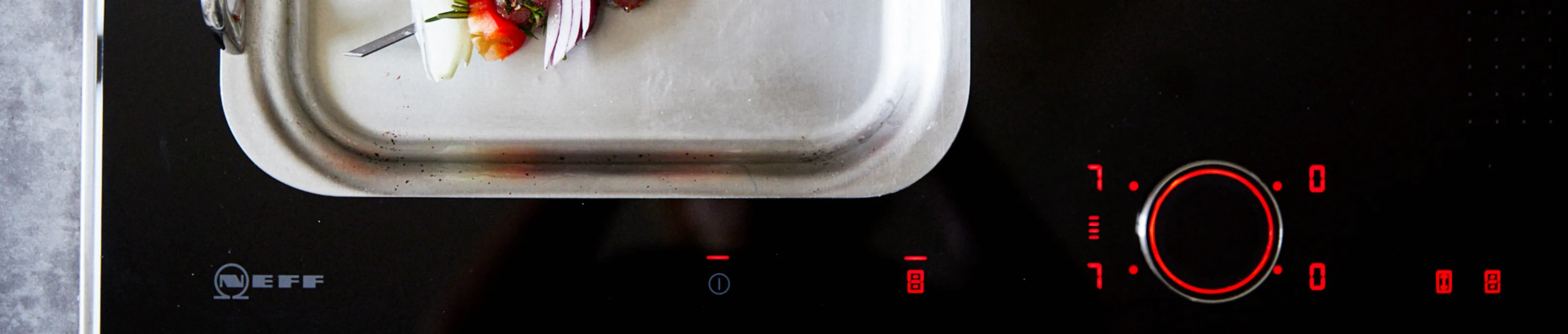 Stainless steel baking tray with fresh strawberries on a black electric stovetop.