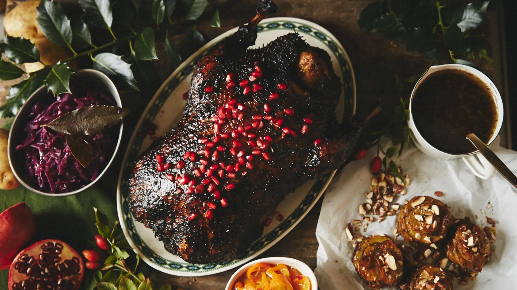 Roasted meat dish garnished with pomegranate seeds, served with side dishes on rustic table.