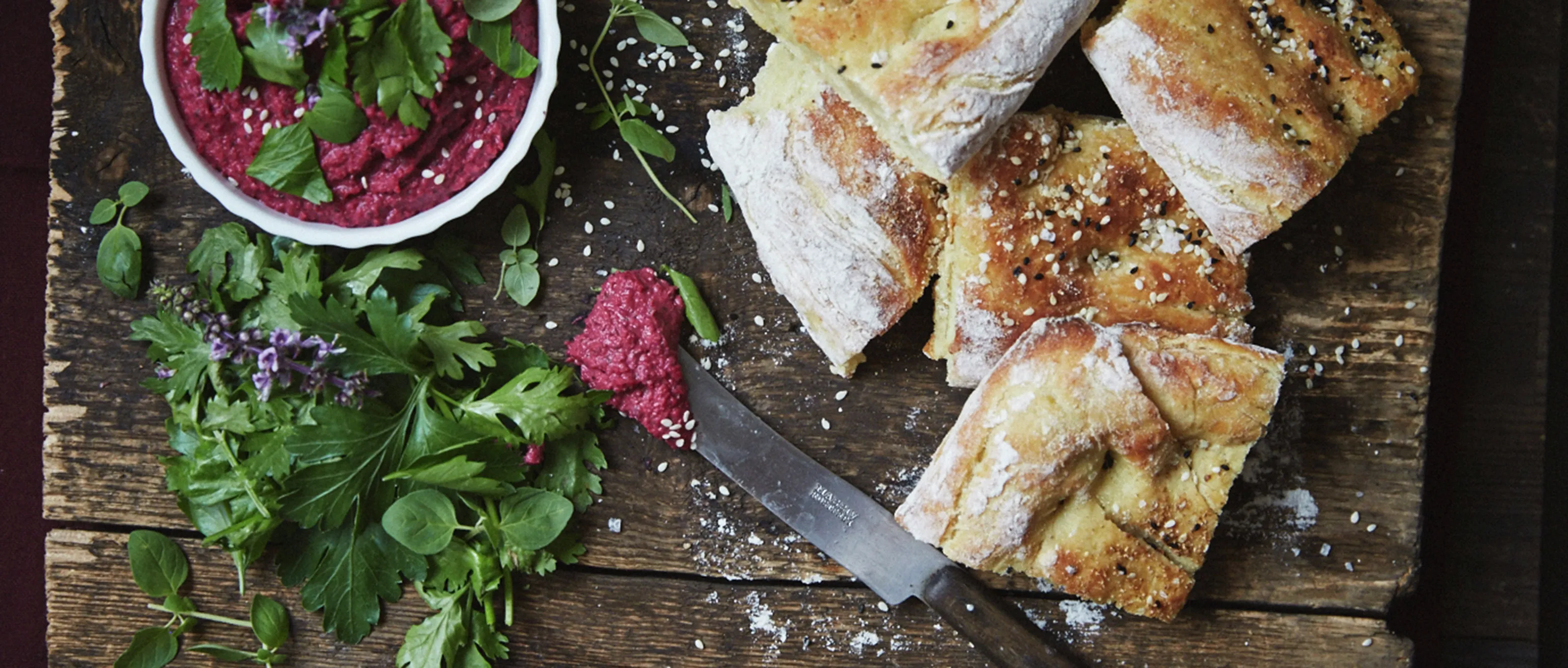 Freshly baked bread, vibrant beet salad, and a knife on a rustic wooden surface.