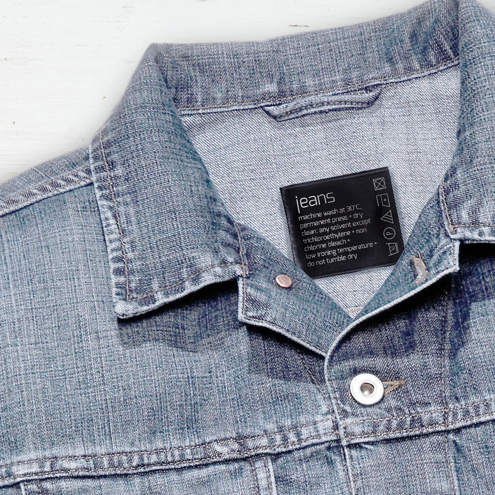 Close-up de o jachetă denim cu o etichetă care indică este făcută din material blugi.