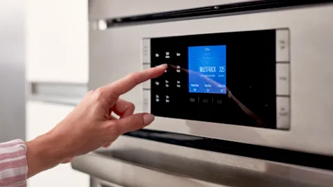 Hand adjusting digital controls on Bosch oven display panel.