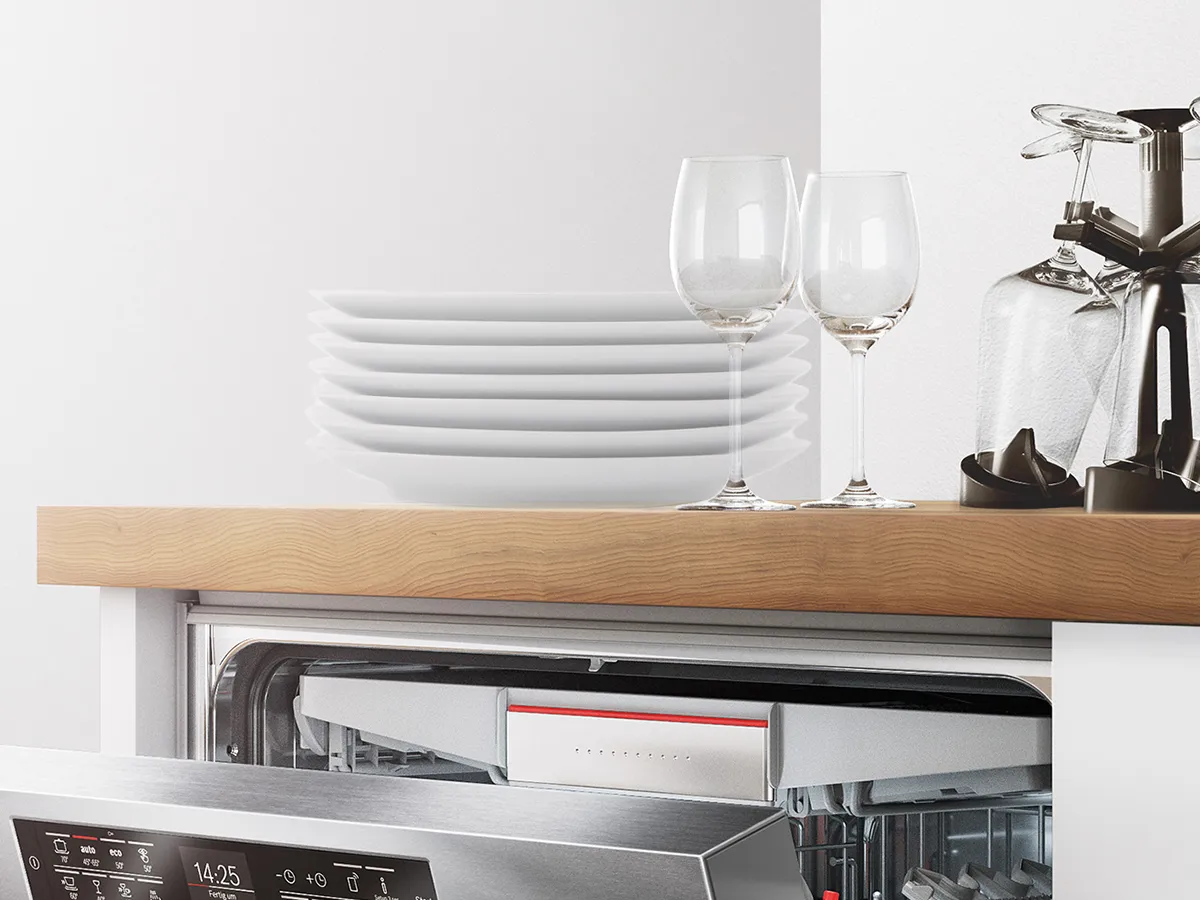Partially open stainless steel dishwasher beneath a wooden countertop holding stacked plates and wine glasses.