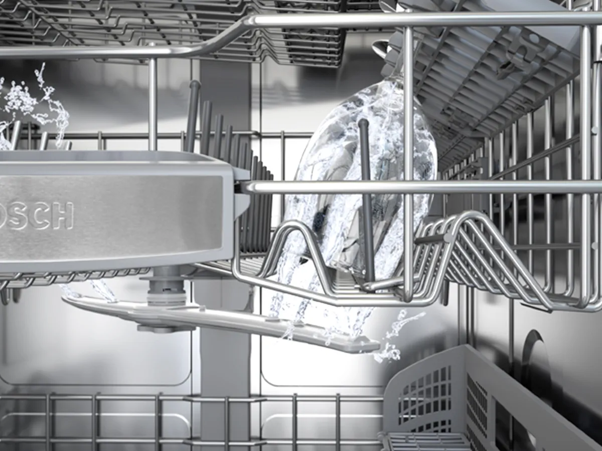 Inside a Bosch dishwasher showing a rotating spray arm spraying water up at a glass on the rack.