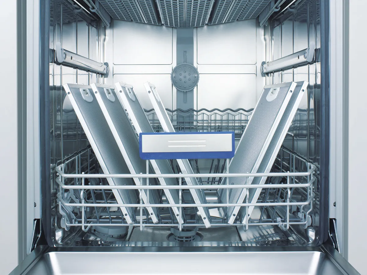 Open dishwasher rack holding rectangular metal mesh cooker hood filters for cleaning.