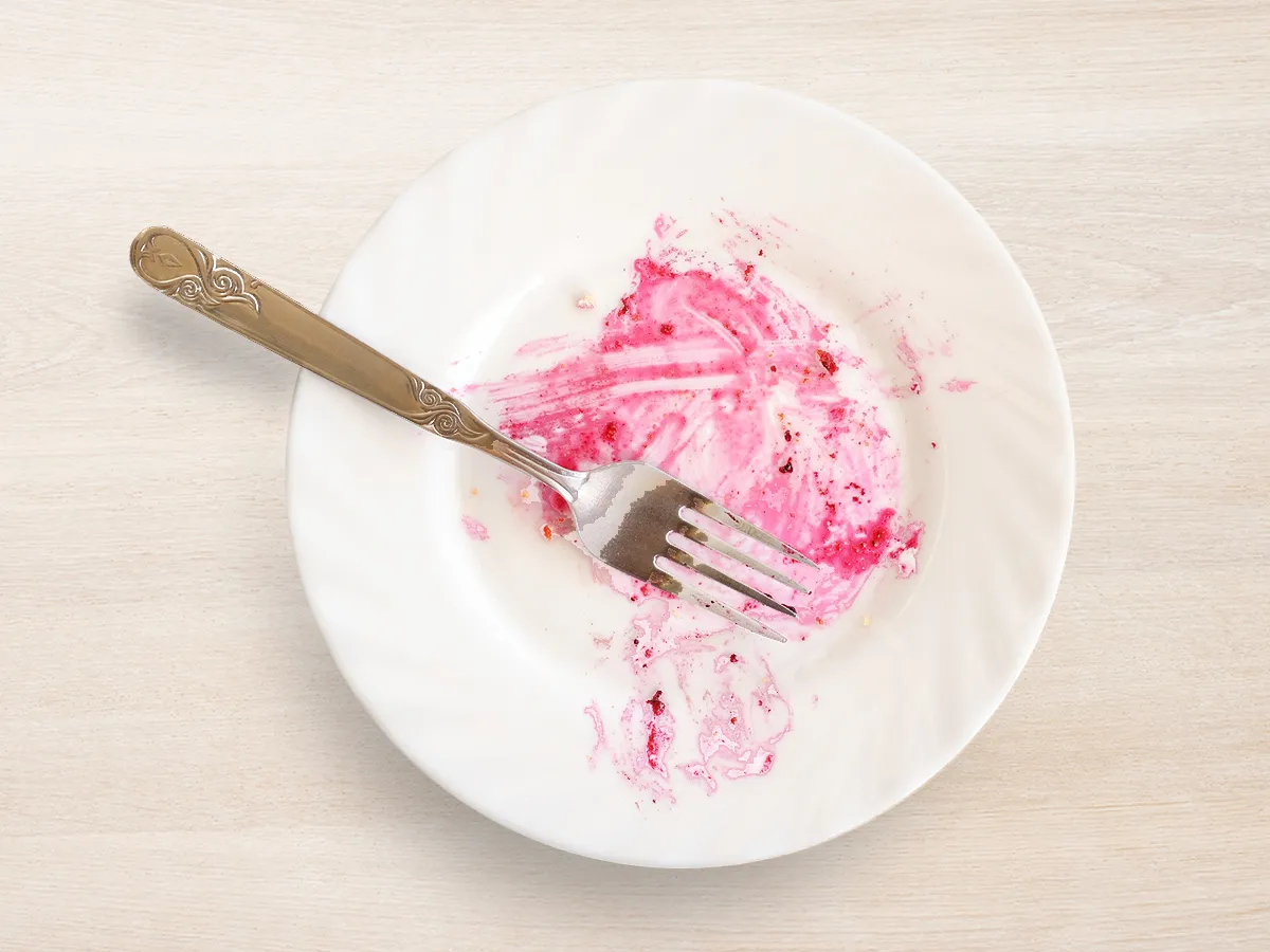 Empty white plate with pink berry sauce stains and a metal fork resting on it.