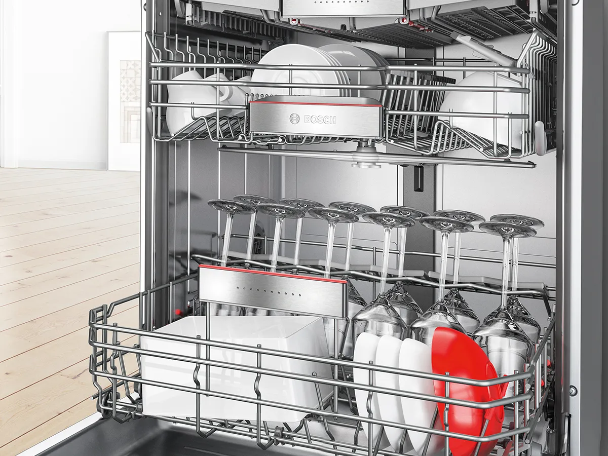 Open Bosch dishwasher loaded with wine glasses, plates, and bowls on adjustable racks.