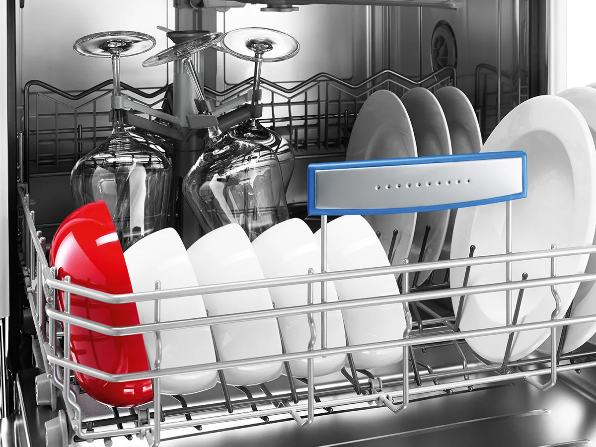 Dishwasher rack holding upside-down wine glasses, white plates, and a row of bowls with a single bright red highlight.