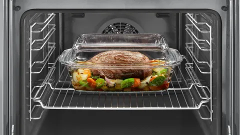 Roast meat with vegetables in a glass baking dish inside an oven