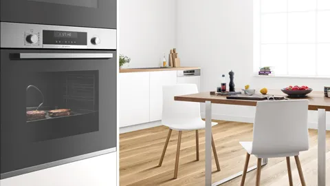 Modern kitchen with built-in oven, white cabinets, wooden floor, and dining table with white chairs