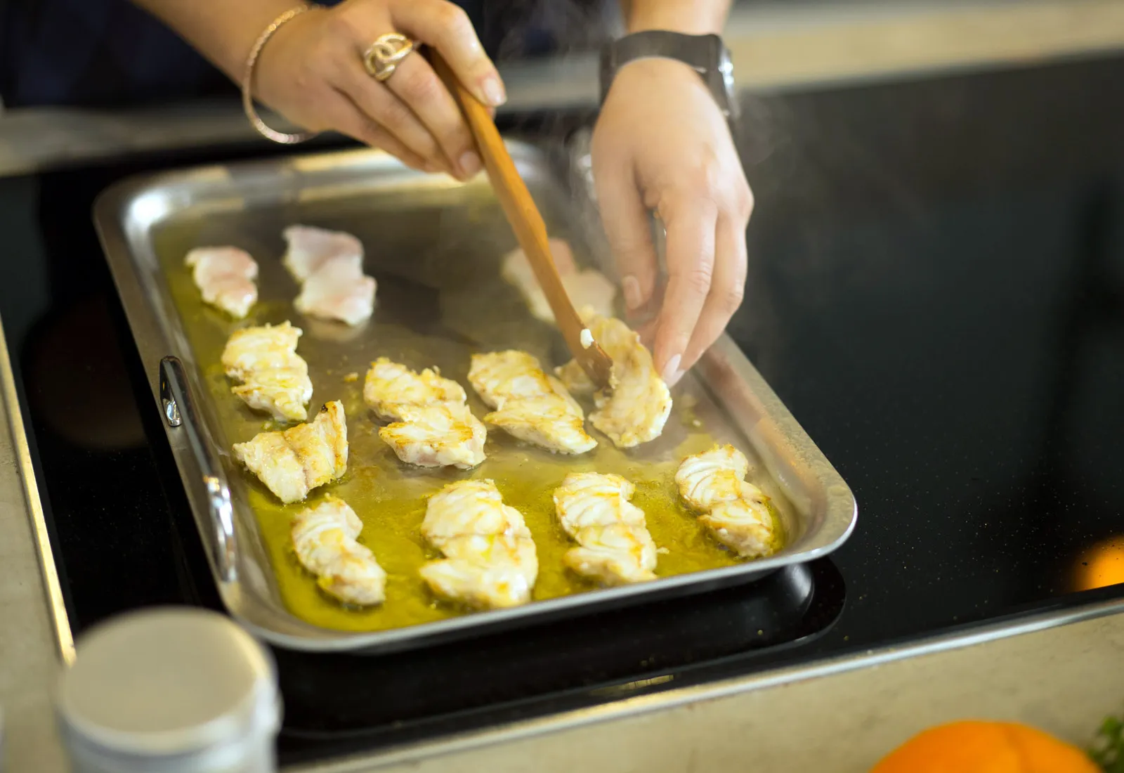 Mani che preparano pezzi di pollo fritti in un piatto di cottura con olio.