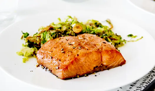 Grilled salmon fillet with black pepper, served with sautéed Brussels sprouts on a white plate.
