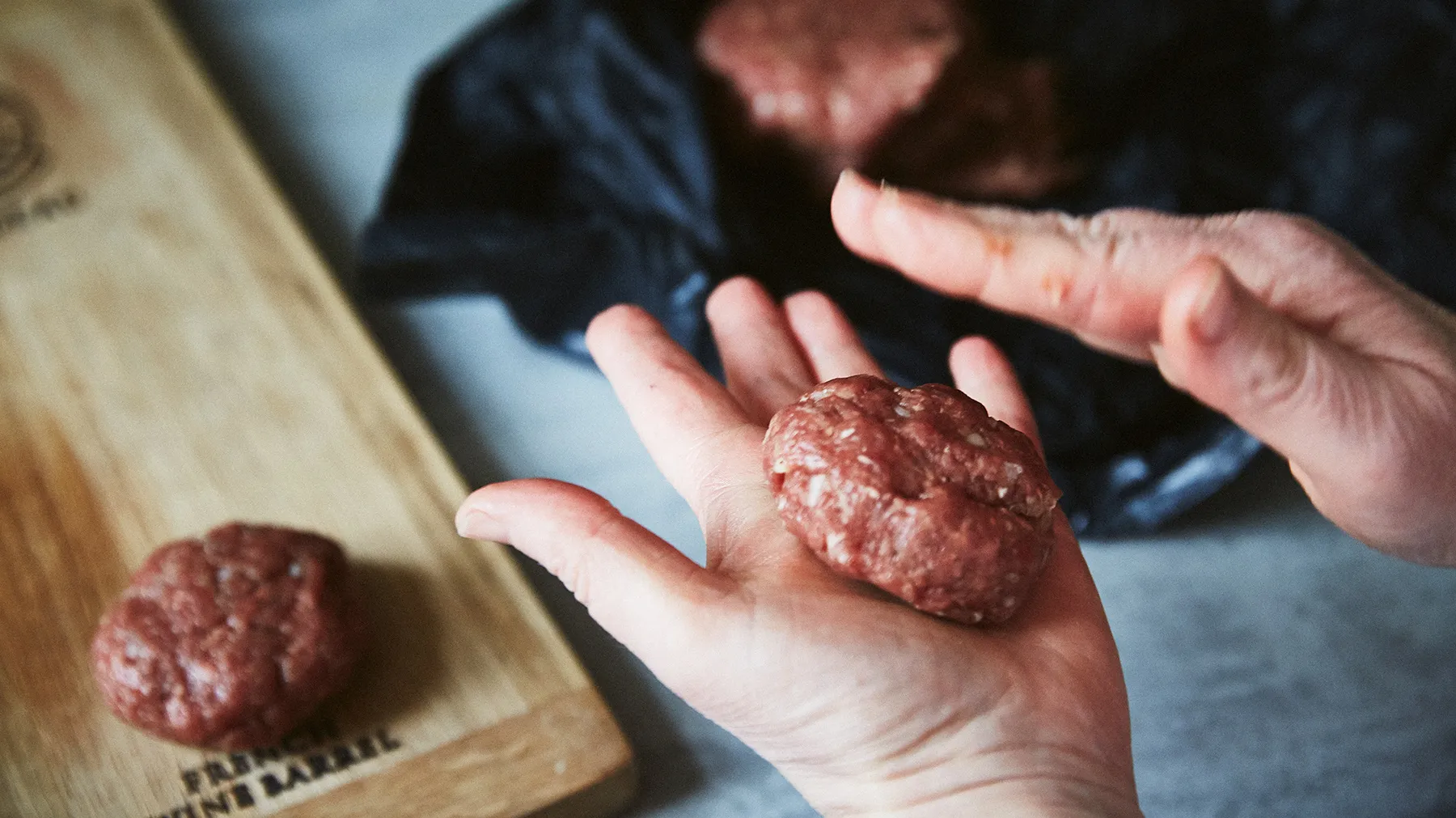 Mani che formano polpette crude su un tagliere di legno.